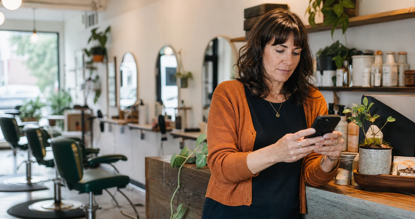 A salon owner checking her phone at the reception counter